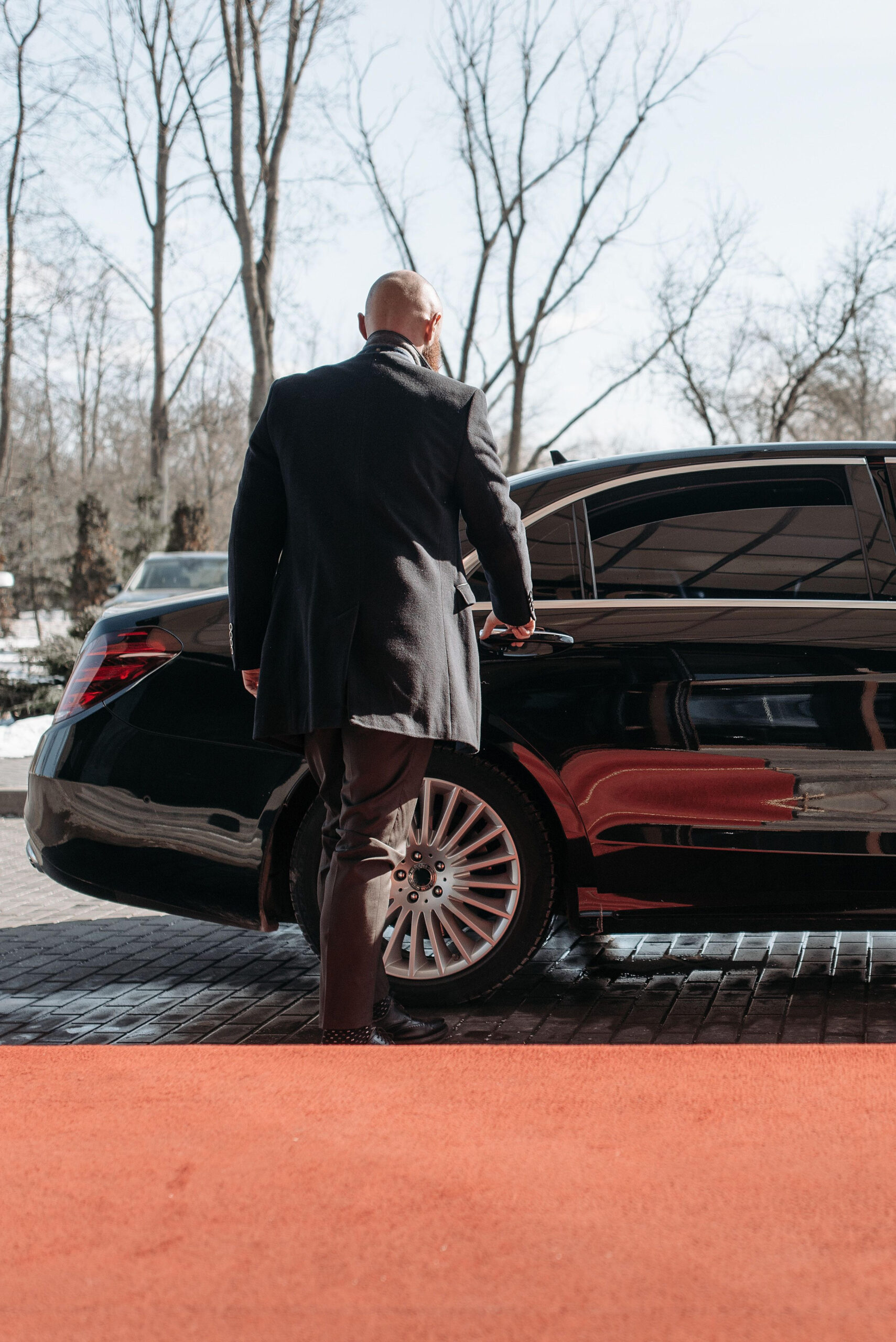 Man in formal attire approaching a black luxury car on a red carpet
